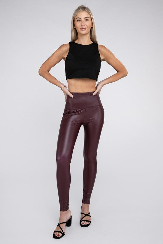 A woman stands confidently wearing a black sleeveless crop top, High Rise Faux Leather Leggings in maroon, and black strappy heels. She has long, straight hair and a neutral background, exuding a sporty and edgy look.