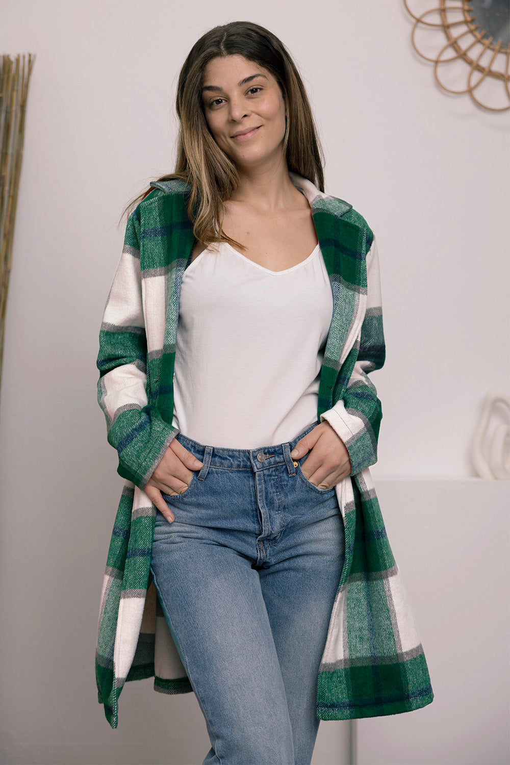 A woman stands on a sidewalk wearing the Double Take Full Size Plaid Button Up Lapel Collar Coat in pink and white over a white top and blue jeans, with her right hand lightly touching her hair. The polyester fabric of the coat makes it durable and perfect for an easy machine wash cold.