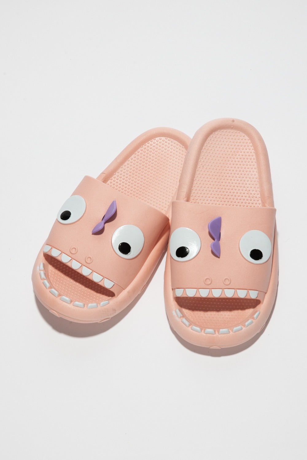 The NOOK JOI Monster Pillow Cloud Slides Non-Slip Slipper features cartoonish monster faces with large eyes, a purple nose, and an open mouth with teeth. Made of durable EVA material, these fun pink cloud slippers also boast an anti-slip design for added safety.