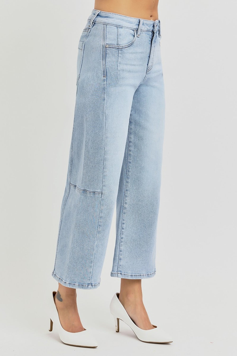 A person wearing RISEN Full Size High Rise Seamed Detail Wide Leg Crop Jeans in light blue and white pointed-toe heels, standing against a plain background.