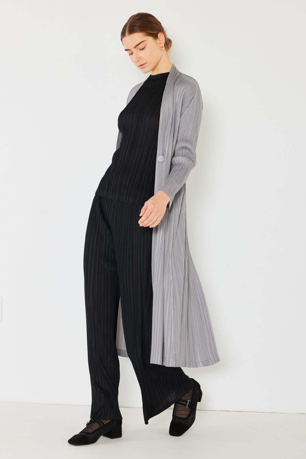 A person wears the Marina West Swim Pleated Long Sleeve Cardigan over a matching top and gray wide-leg pants, standing against a plain light background. This versatile layering piece, with its chic pleated long sleeves, adds an elegant touch to the ensemble.