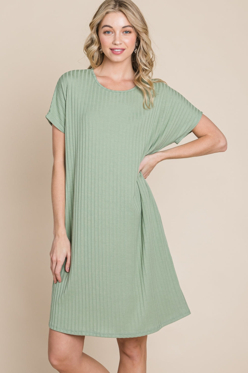 Against a beige background, a person is dressed in the BOMBOM Ribbed Round Neck Short Sleeve Dress in green, featuring a pocket.