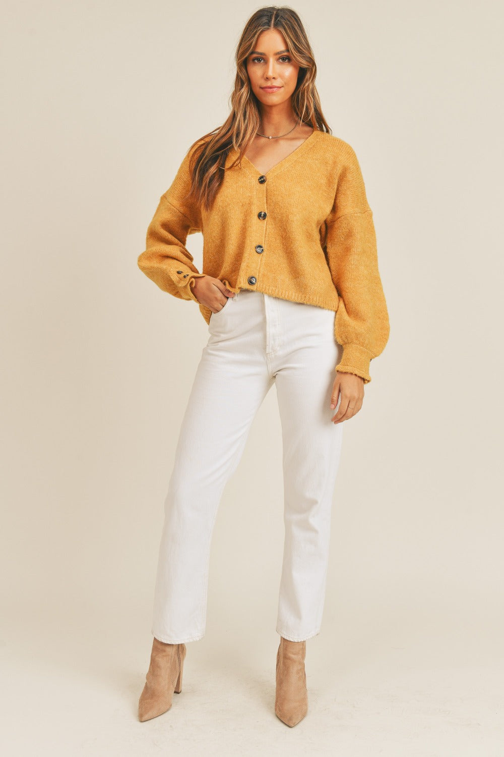 A person wears the MABLE Long Sleeve Button Down Sweater Cardigan in mustard, paired with white high-waisted pants, standing in front of a plain background.