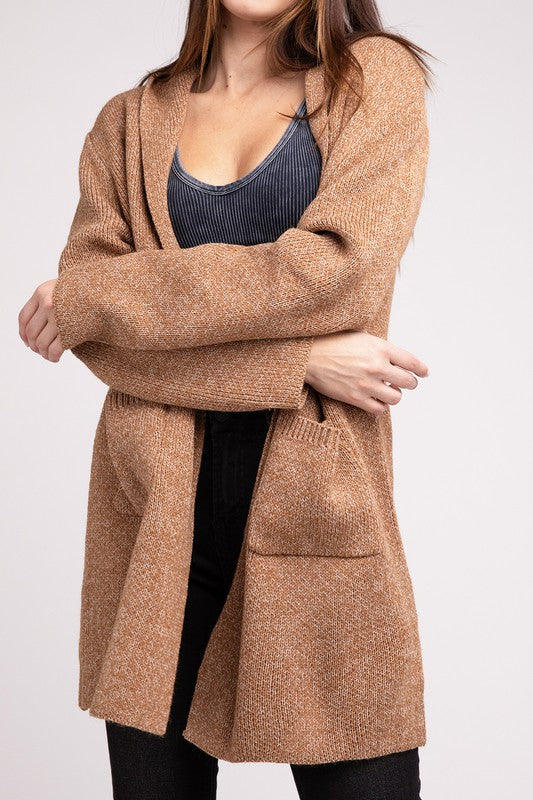 A woman modeling a cozy Hooded Open Front Sweater Cardigan over a black top, posing with one hand in her pocket against a gray background.