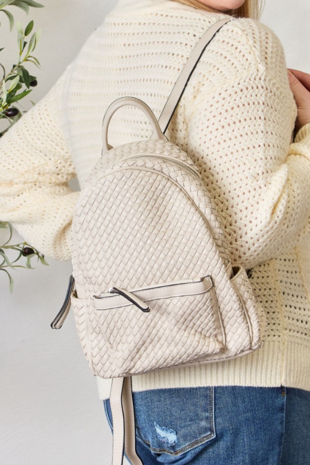 A person wearing a cream sweater and jeans is carrying the SHOMICO PU Leather Woven Backpack in brown.