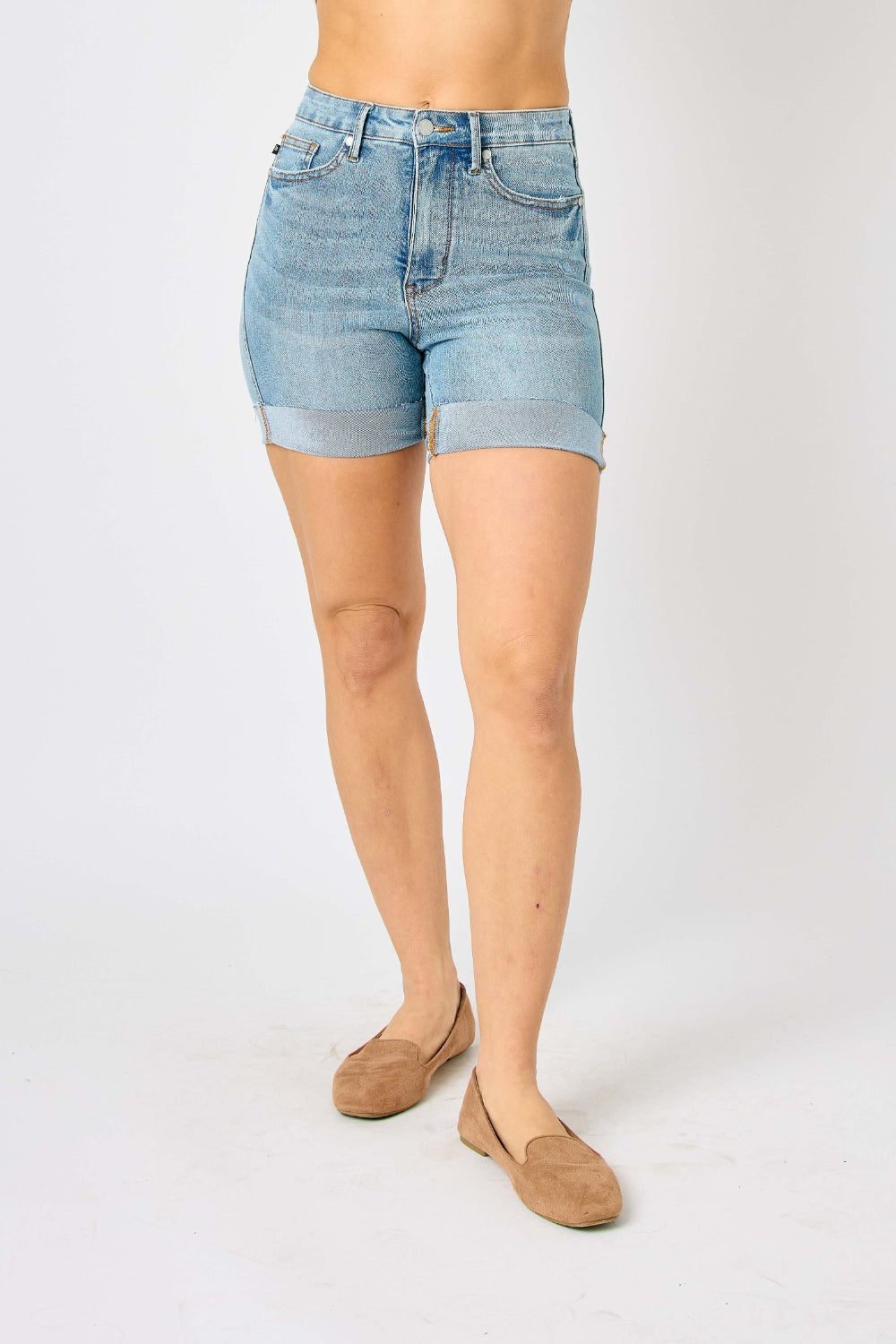 Person wearing Judy Blue Full Size Tummy Control Denim Shorts, which have a flattering fit, paired with brown shoes against a plain white background.