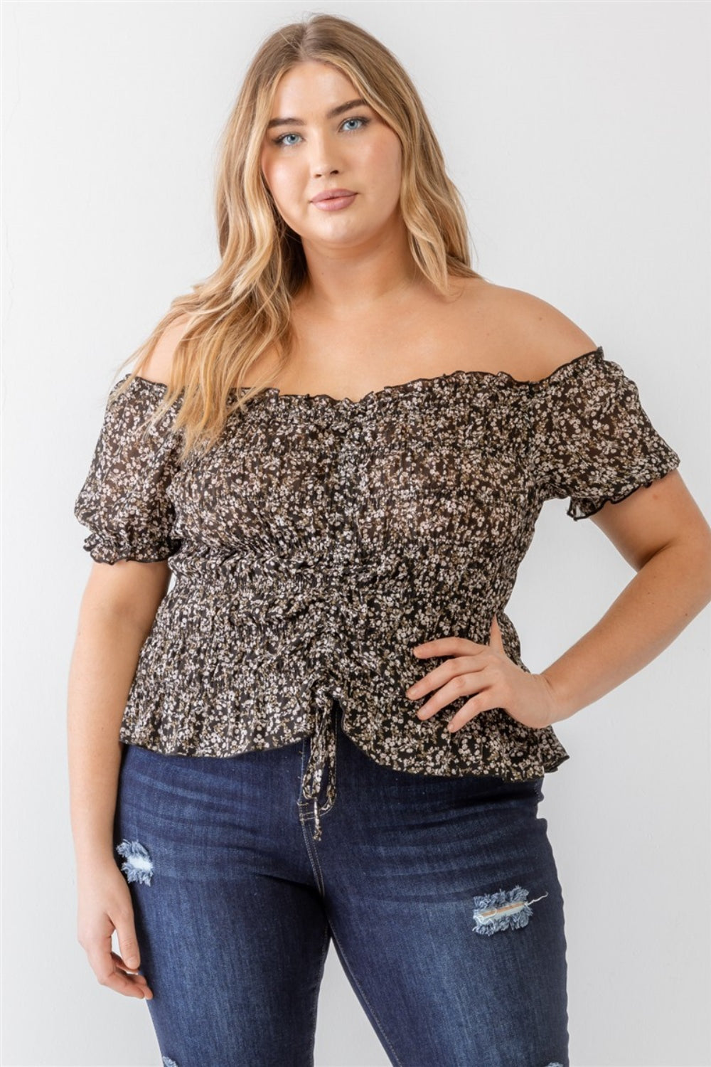 Wearing the Zenobia Plus Size Frill Ruched Off-Shoulder Short Sleeve Blouse and ripped jeans, a person with long hair poses against a plain white background.