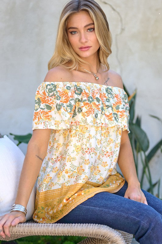 A woman with blonde hair is smiling while standing outdoors, wearing the Printed Off Shoulder Smocked Top paired with jeans.