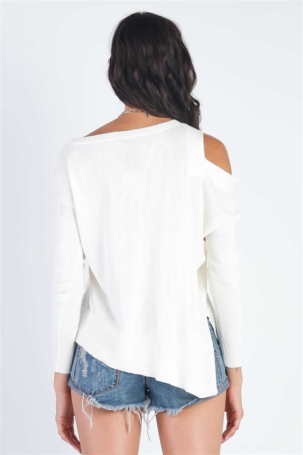 A person wearing the UNIQ Cold Shoulder Long Sleeve Knit Top in black and distressed denim shorts stands against a plain white background, effortlessly showcasing a versatile wardrobe choice.