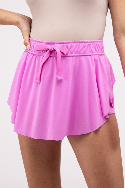 A person wearing a Ruffle Hem Tennis Skirt with Hidden Inner Pockets in vibrant pink, featuring a drawstring waist and showing only the lower torso and upper legs.