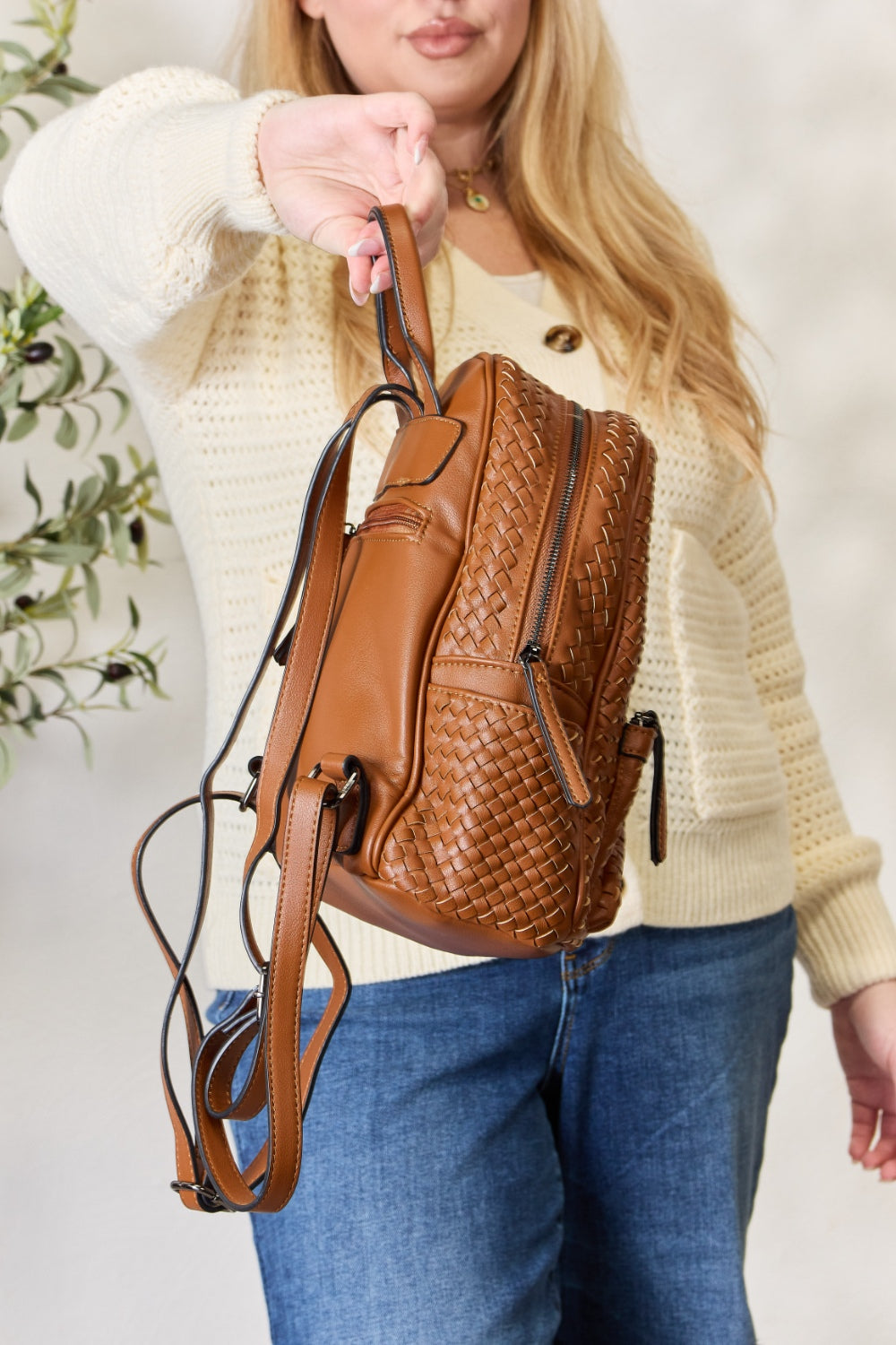 A person wearing a cream sweater and jeans is carrying the SHOMICO PU Leather Woven Backpack in brown.