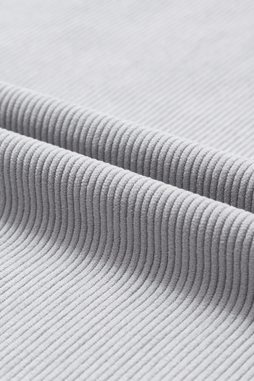A woman wearing the Light Grey Ribbed Corduroy Oversized Sweatshirt with loose long sleeves, designed in corded fabric, making it fashionable for all body shapes.
