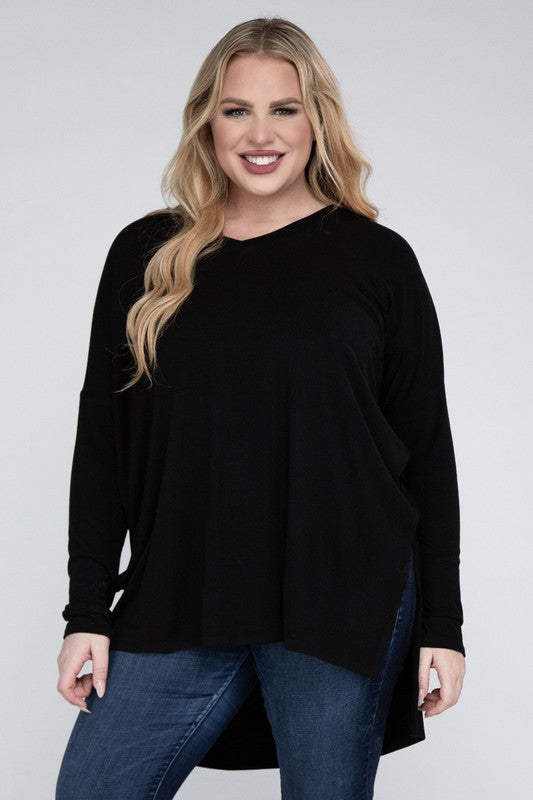 A woman with long, blonde hair wears a Plus Dolman Sleeve V-Neck Side Slit Hi-Low Hem Top and blue jeans, posing with one hand on her hip and smiling at the camera.