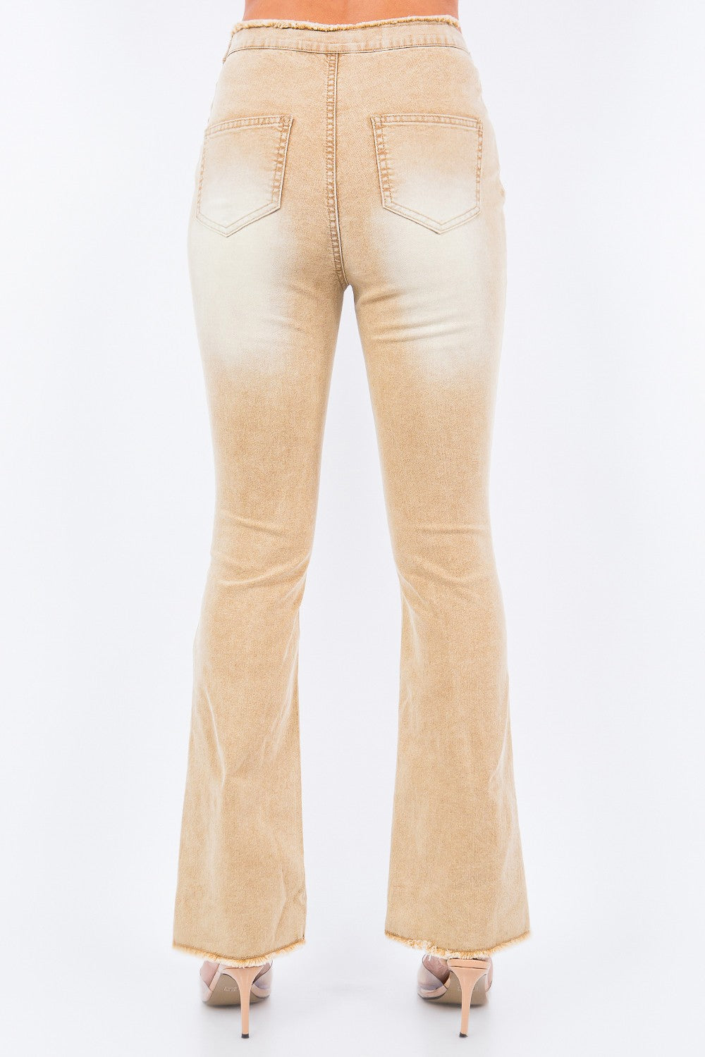 A person is wearing American Bazi V-Cut Ruched Flare Pants in light beige with frayed hems, paired with transparent high-heeled sandals.