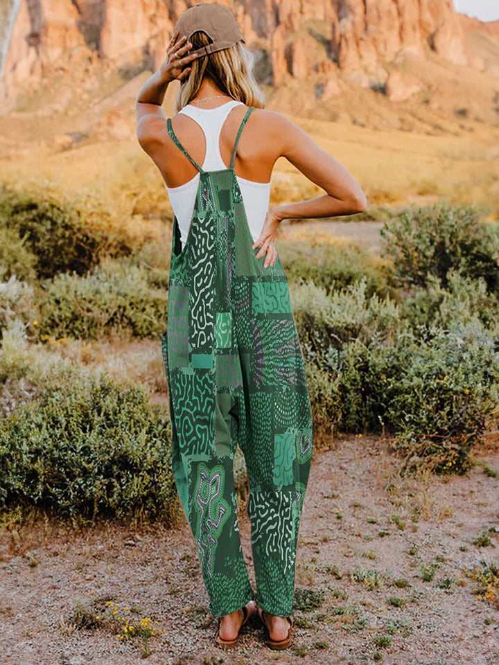 A person standing outdoors in front of rocky terrain, wearing a Full Size Printed V-Neck Sleeveless Jumpsuit and a hat.