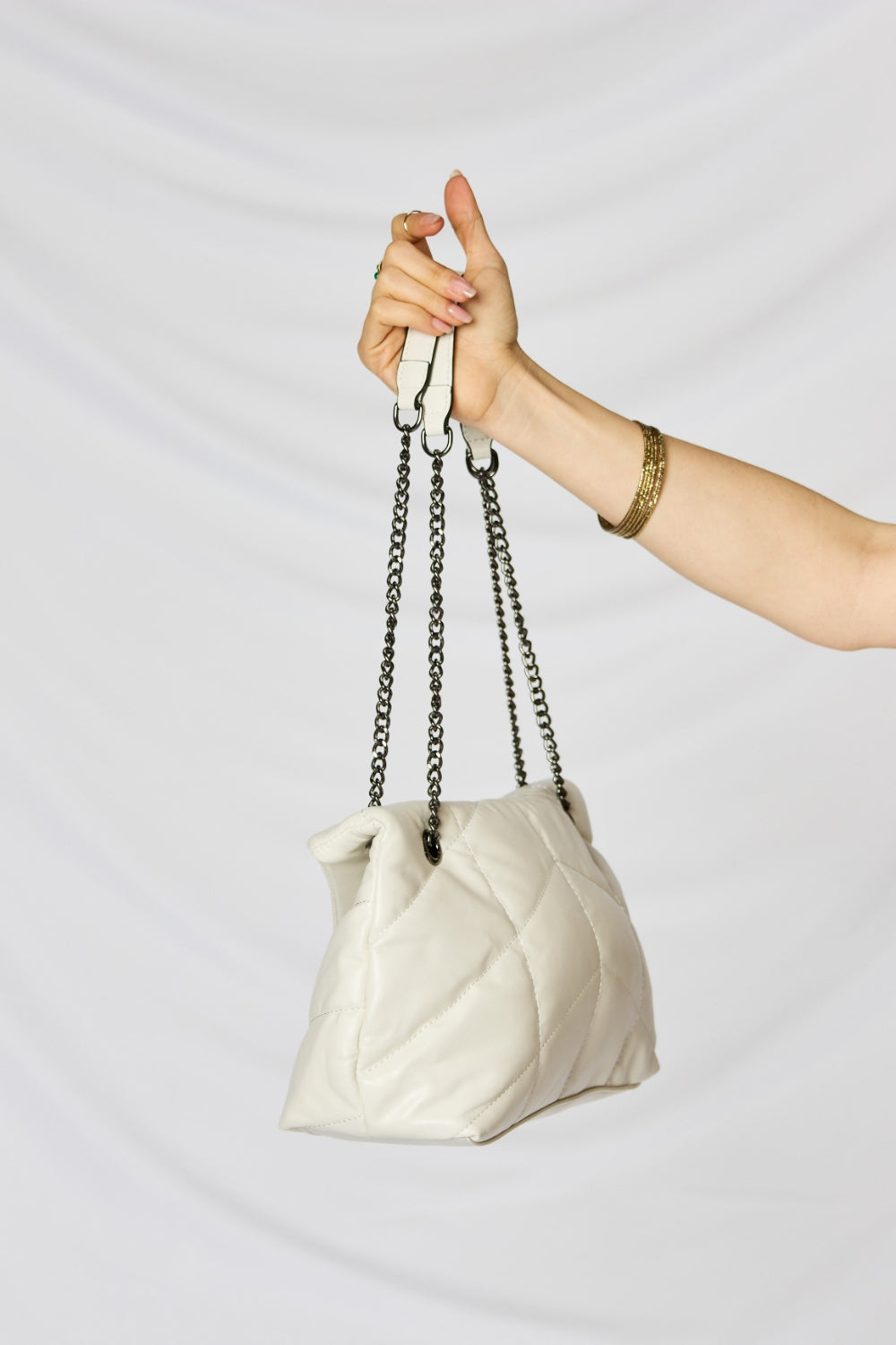 A person holding a stylish SHOMICO PU Leather Chain Handbag over their shoulder against a white background. They are dressed in a beige outfit and looking at the camera, embodying sustainable fashion.