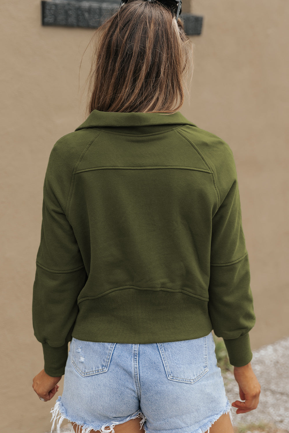 A person with long, wavy hair stands in front of a white and black background, wearing the Green Fleece Lined Zip Up Stand Collar Thumbhole Sleeve Sweatshirt paired with white shorts, creating a stylish look perfect for casual outings.