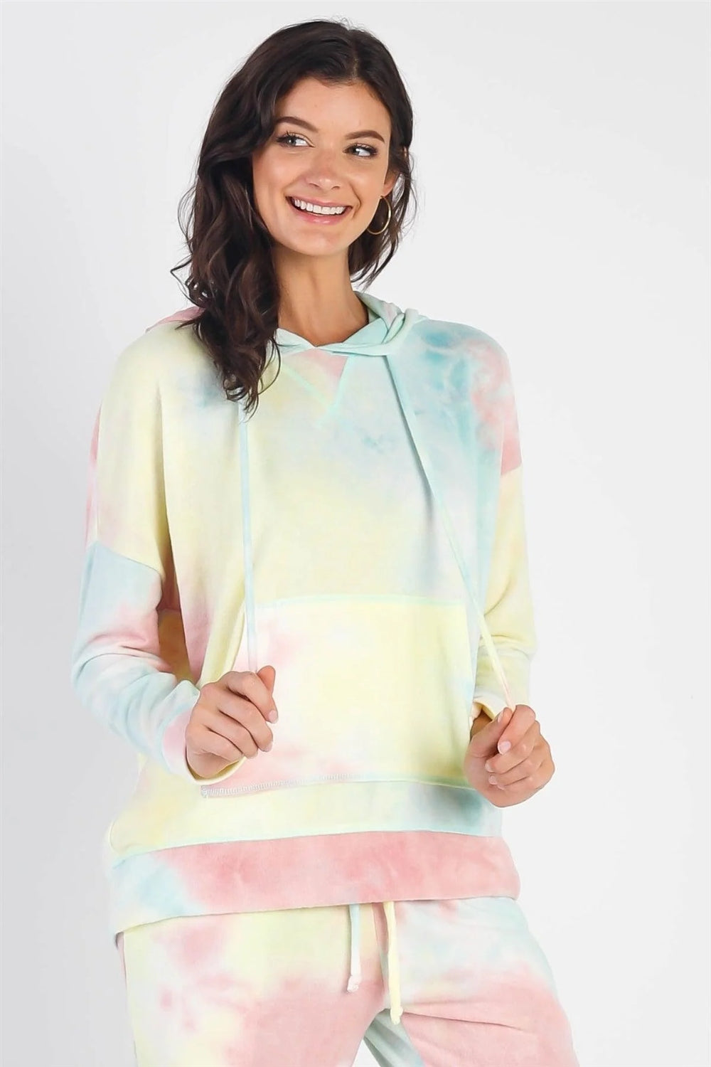 A person smiles while wearing the Cherish Apparel Drawstring Tie-Dye Dropped Shoulder Hoodie and matching pants, exuding a bohemian vibe while standing against a plain background.