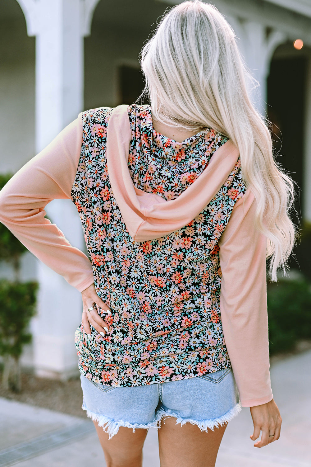 A person with long blonde hair wears a Pink Floral Patch Half Zip Kangaroo Pocket Hoodie and denim shorts, standing outdoors with their back facing the camera.