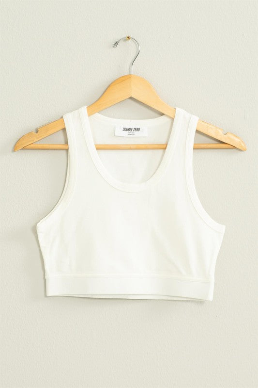 The "All I Need Cropped Tank Top," featuring a light blue hue and a fitted silhouette, hangs on a wooden hanger against a white wall.