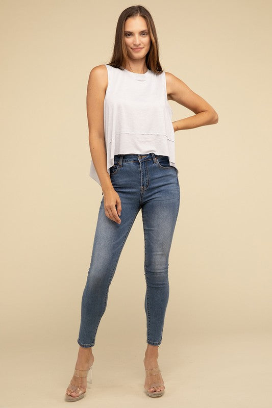 Wearing the Shark Bite Side Slit Short Sleeveless Top in maroon paired with white pants, a model is set against a beige background, exemplifying an effortlessly chic and casual wardrobe.