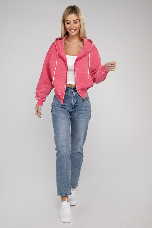 A smiling woman wearing a pink Acid Wash Cropped Zip-Up Hoodie and blue jeans, posing with one hand adjusting her hood.