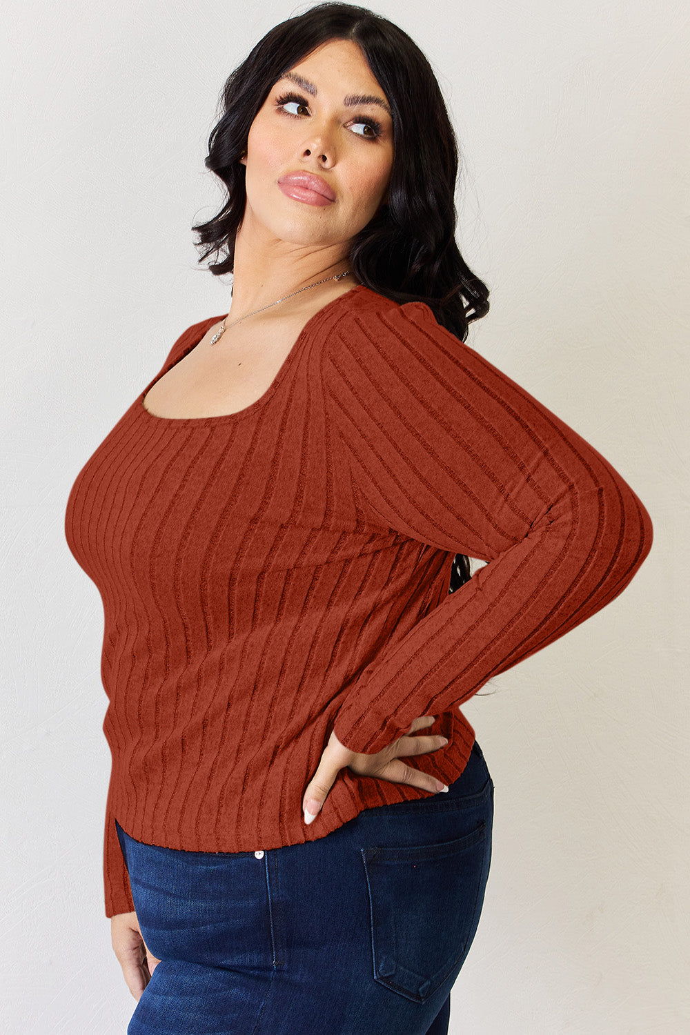 A person is standing and smiling, wearing the Basic Bae Full Size Ribbed Long Sleeve T-Shirt in light brown along with jeans. The basic style is perfect for any casual outing.