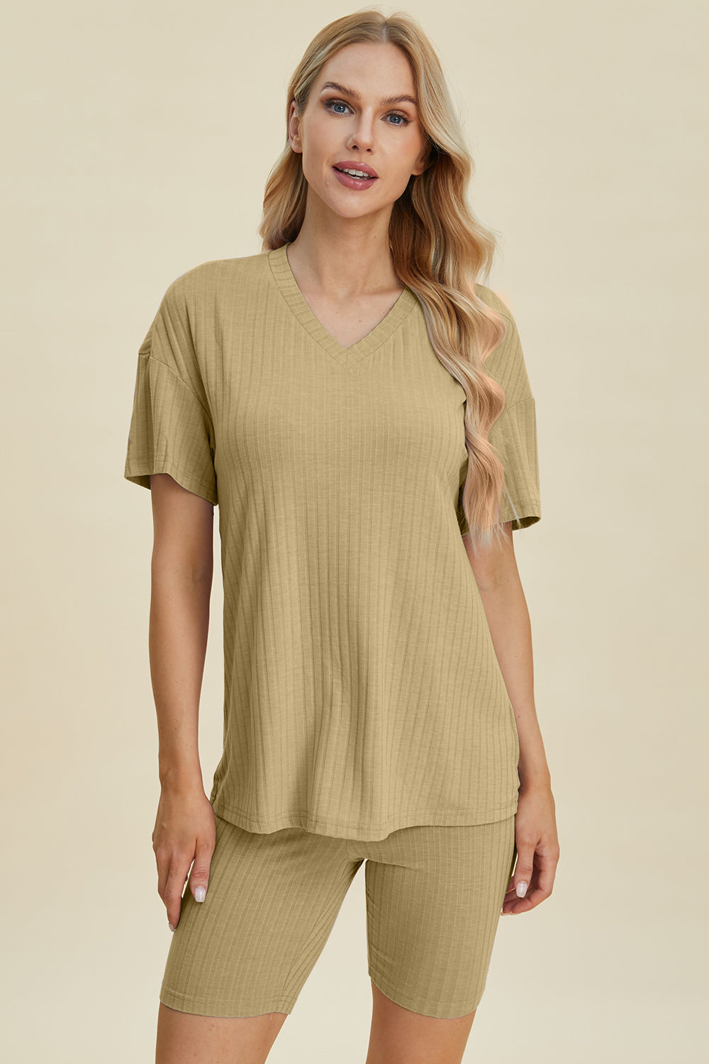 A woman with long blonde hair wearing the Basic Bae Full Size Ribbed V-Neck Short Sleeve Top and Shorts Set in rust stands against a plain background. This stylish two-piece set is made from a comfortable, stretchy fabric that is also machine washable.