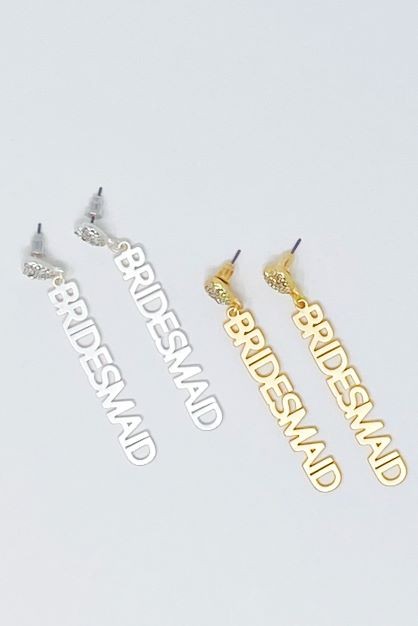 A pair of silver and a pair of gold-plated brass "Be My Bridesmaid" slogan earrings against a light background.