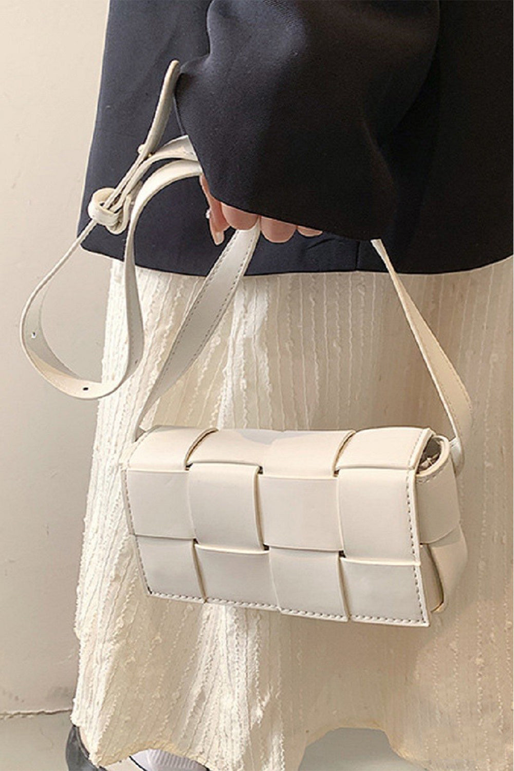 Person wearing a white button-up shirt and holding a black Zenana Vegan Leather Woven Crossbody Bag.