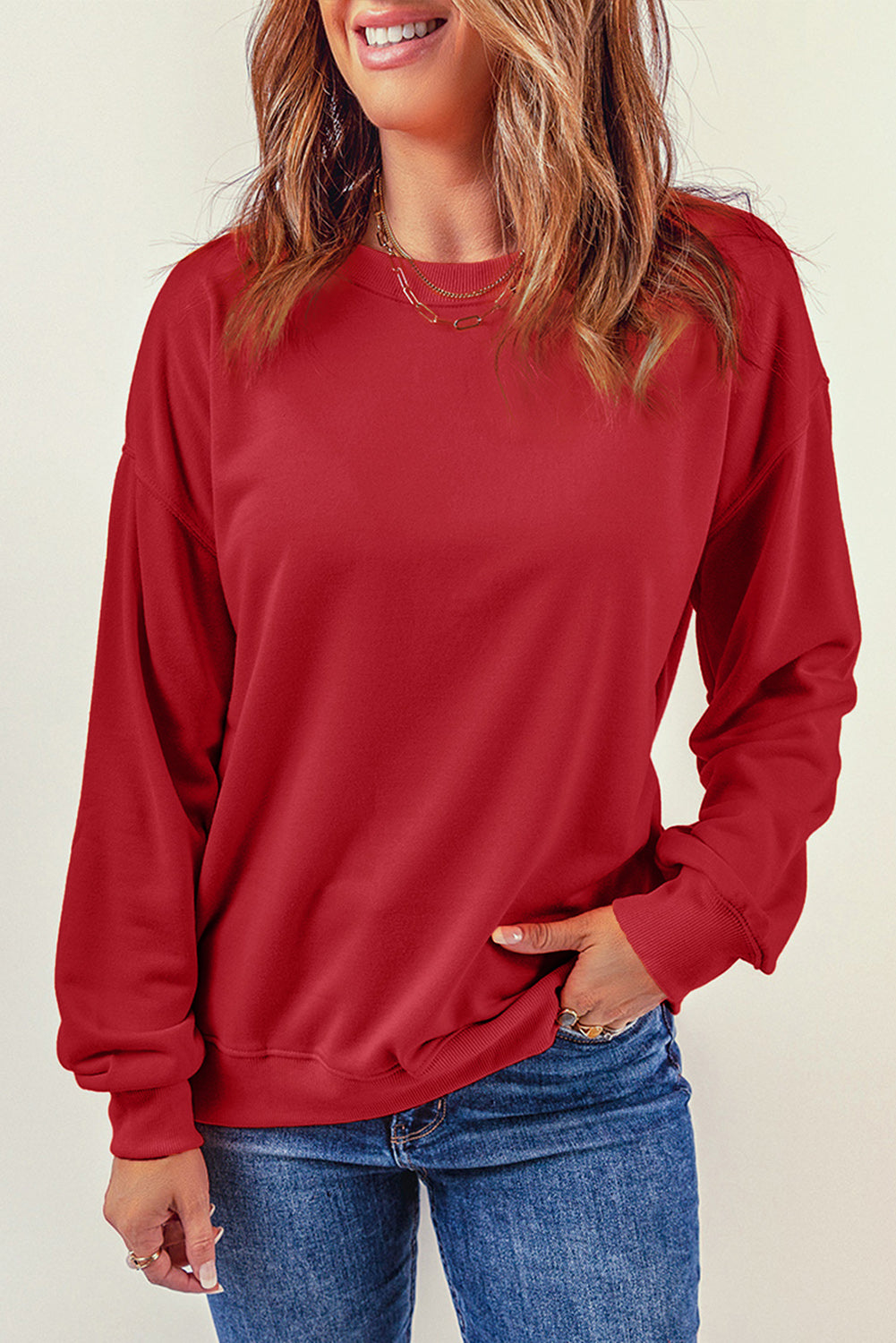 A person wearing a long-sleeved red shirt and blue jeans stands with their back to the camera, one hand resting on their hip, as if showcasing a cozy Fiery Red Plain Crew Neck Pullover Sweatshirt for winter.