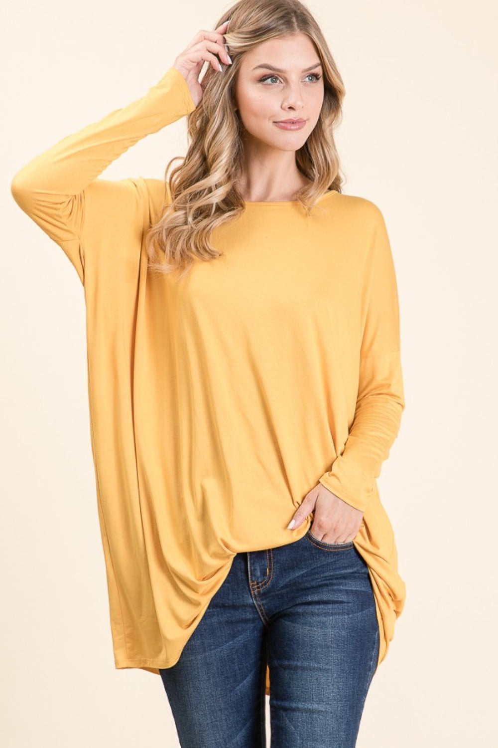 A woman with long blonde hair is wearing a versatile and comfortable, loose-fitting BOMBOM Round Neck Long Sleeve Oversized Top in yellow and blue jeans. She is smiling and standing against a plain light background.