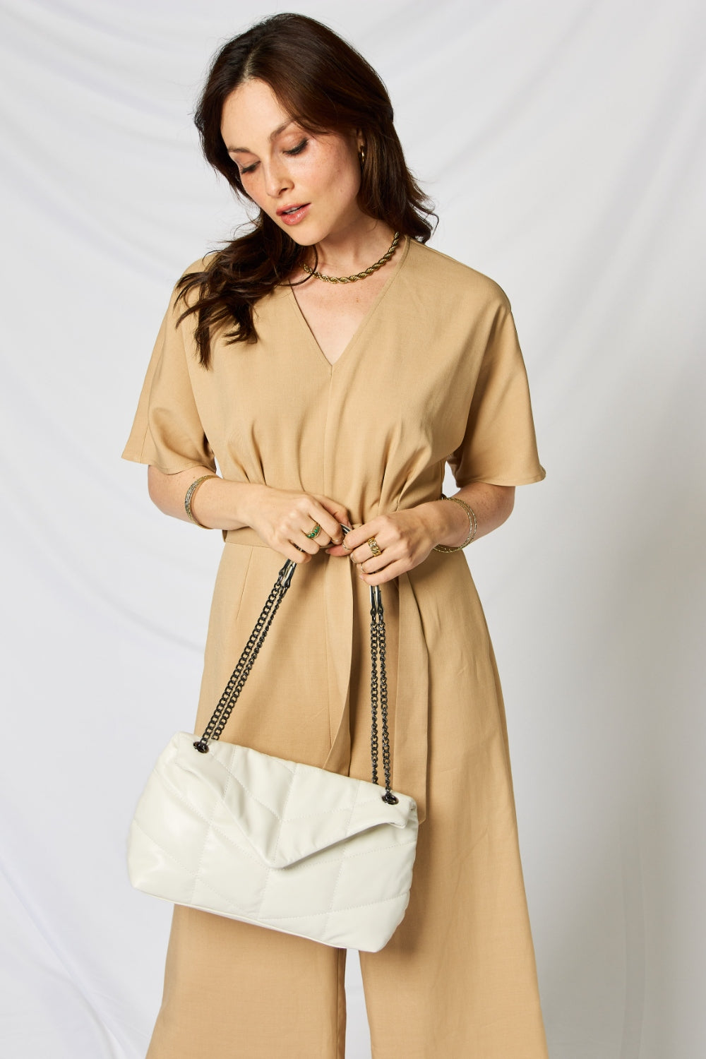 A person holding a stylish SHOMICO PU Leather Chain Handbag over their shoulder against a white background. They are dressed in a beige outfit and looking at the camera, embodying sustainable fashion.