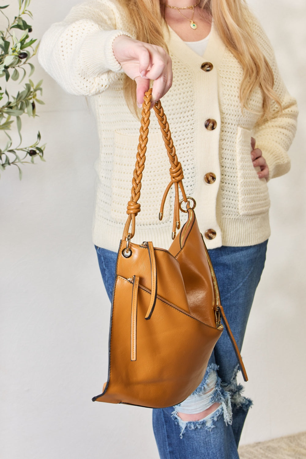 A person in a cream sweater holds a medium-size SHOMICO Zipper Detail Shoulder Bag with gold metal zipper pockets.