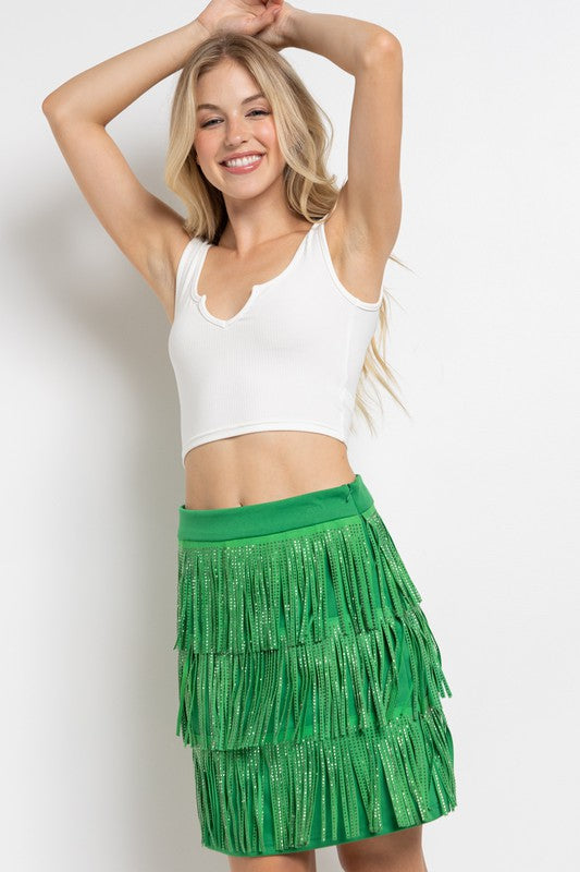 Close-up of the RHINESTONE SUEDE FRINGE SKIRT in pink, featuring a person’s hand resting lightly on the skirt adorned with rhinestone fringes.