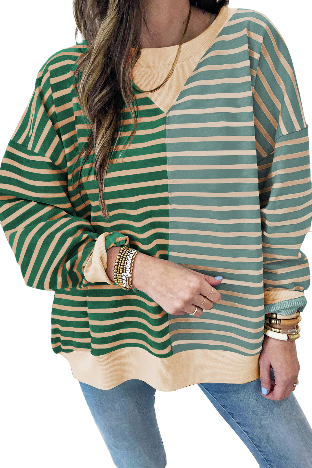 A woman with long hair is wearing a Green Stripe Casual Stripe Colorblock Drop Shoulder Oversize Sweatshirt, blue ripped jeans, and multiple bracelets, walking in front of a shiplap wall.