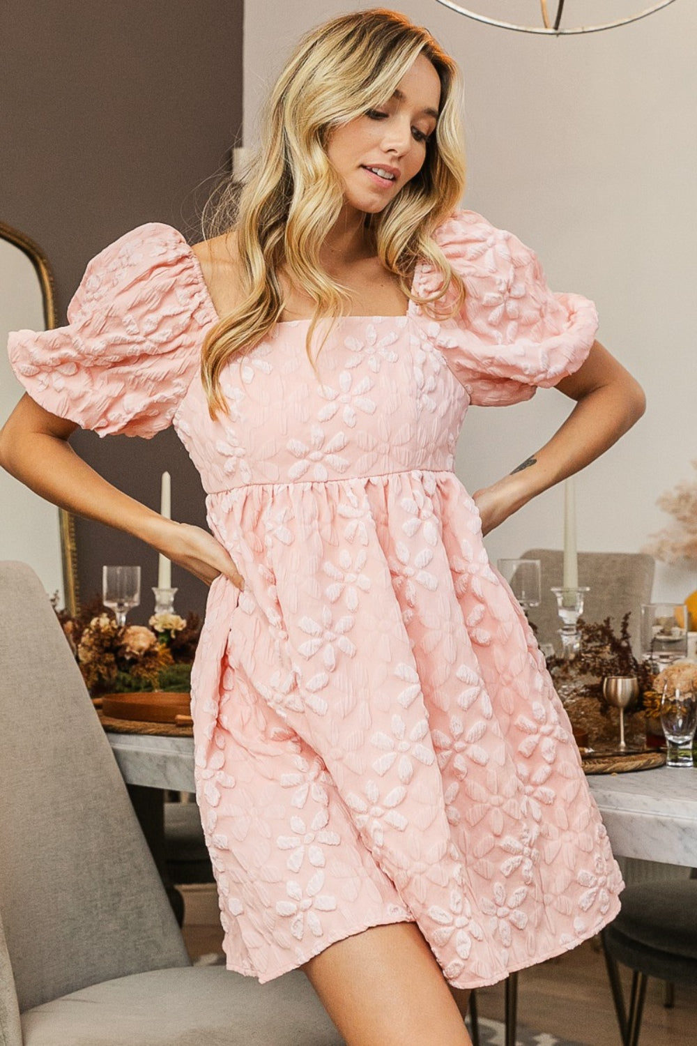 A woman in the BiBi Flower Square Neck Puff Sleeve Dress stands indoors near a set dining table, showcasing its romantic and feminine floral details.