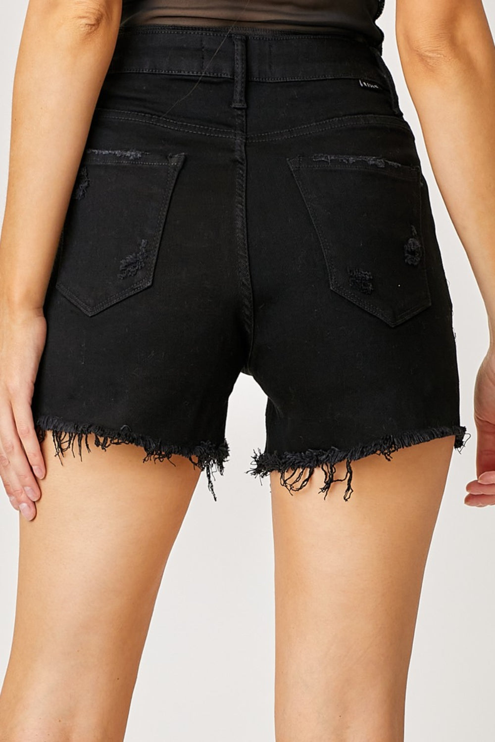 A person wearing RISEN Frayed Hem Denim Shorts with Fringe Detail Pockets, featuring decorative chains hanging from the front pockets, perfect for summer fashion. The high-waisted shorts have a distressed look with a frayed hem and fringe detail pockets for an edgy style.