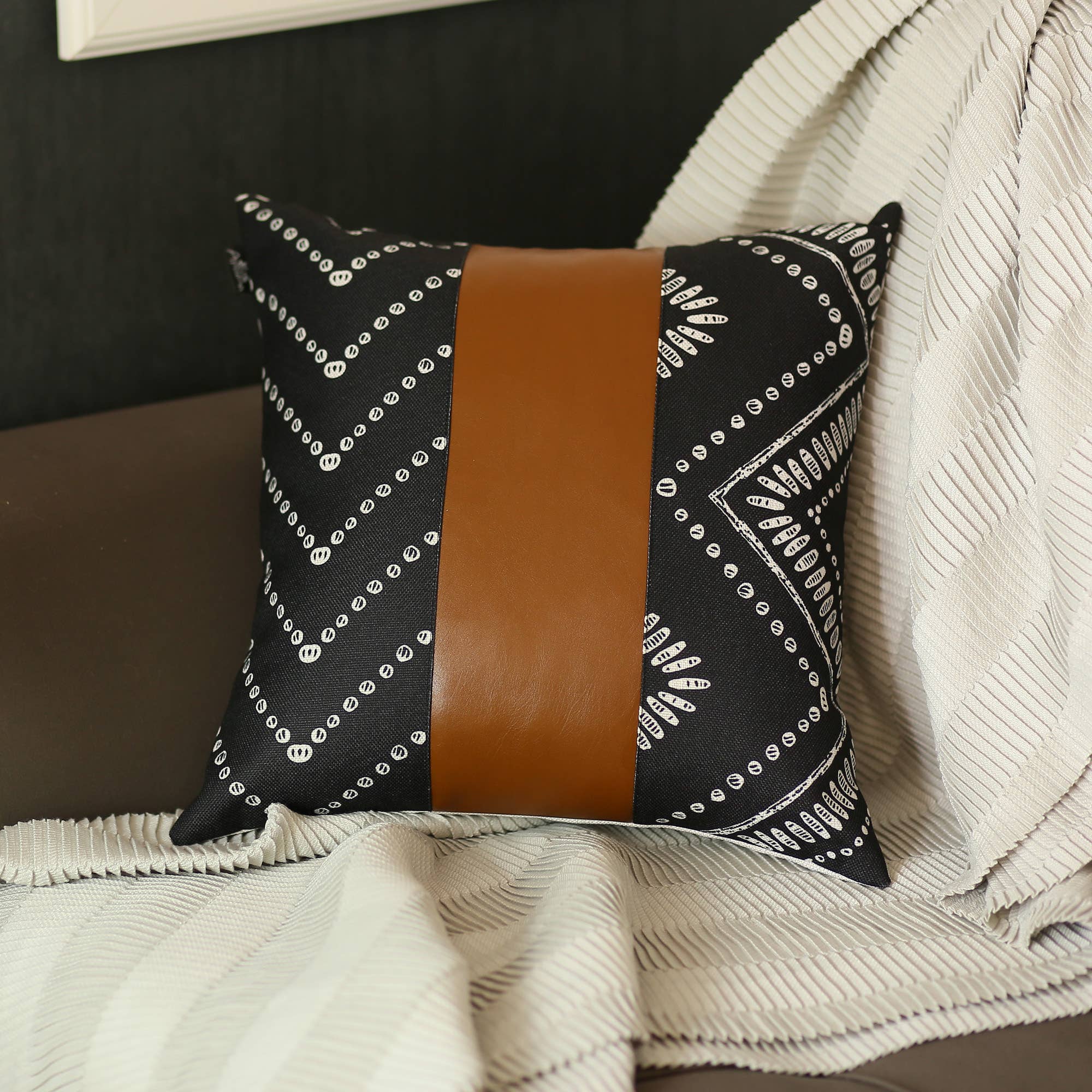 A Boho Handcrafted Decorative Single Throw Pillow Cover, adorned with white geometric patterns and a central band of vegan faux leather, rests elegantly on a beige textured blanket.