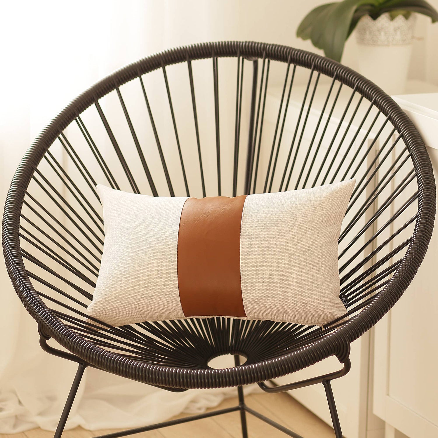 In a well-lit room, a black wire chair is tastefully adorned with a Boho Handcrafted Decorative Single Throw Pillow Cover in beige and brown, featuring vegan faux leather.