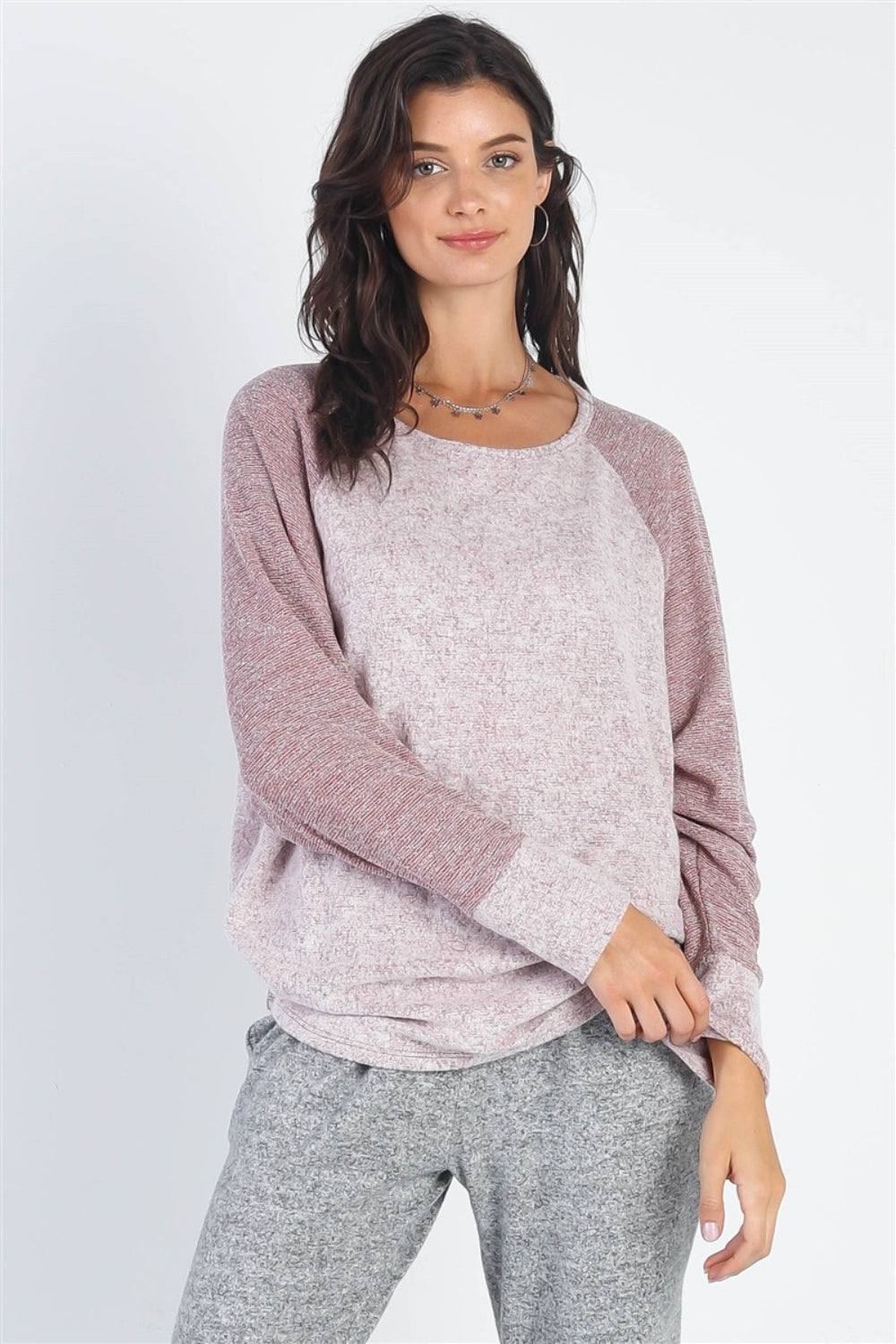 A woman stands wearing the Cherish Apparel Round Neck Long Sleeve Contrast Top in pink and gray with matching gray pants, set against a plain background.