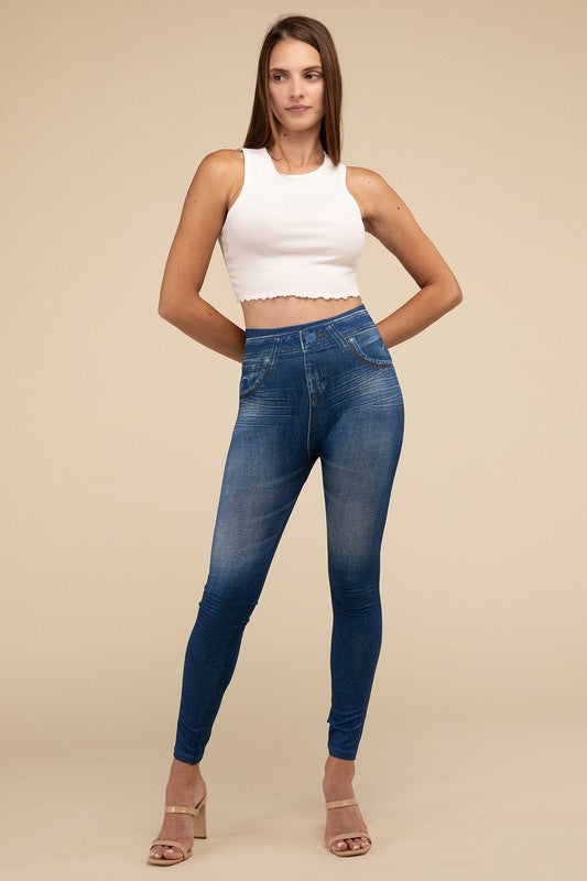 A person wearing Denim Leggings in a high-waisted black design and paired with black heels poses against a plain beige background, highlighting the sleek, stretchy fit.