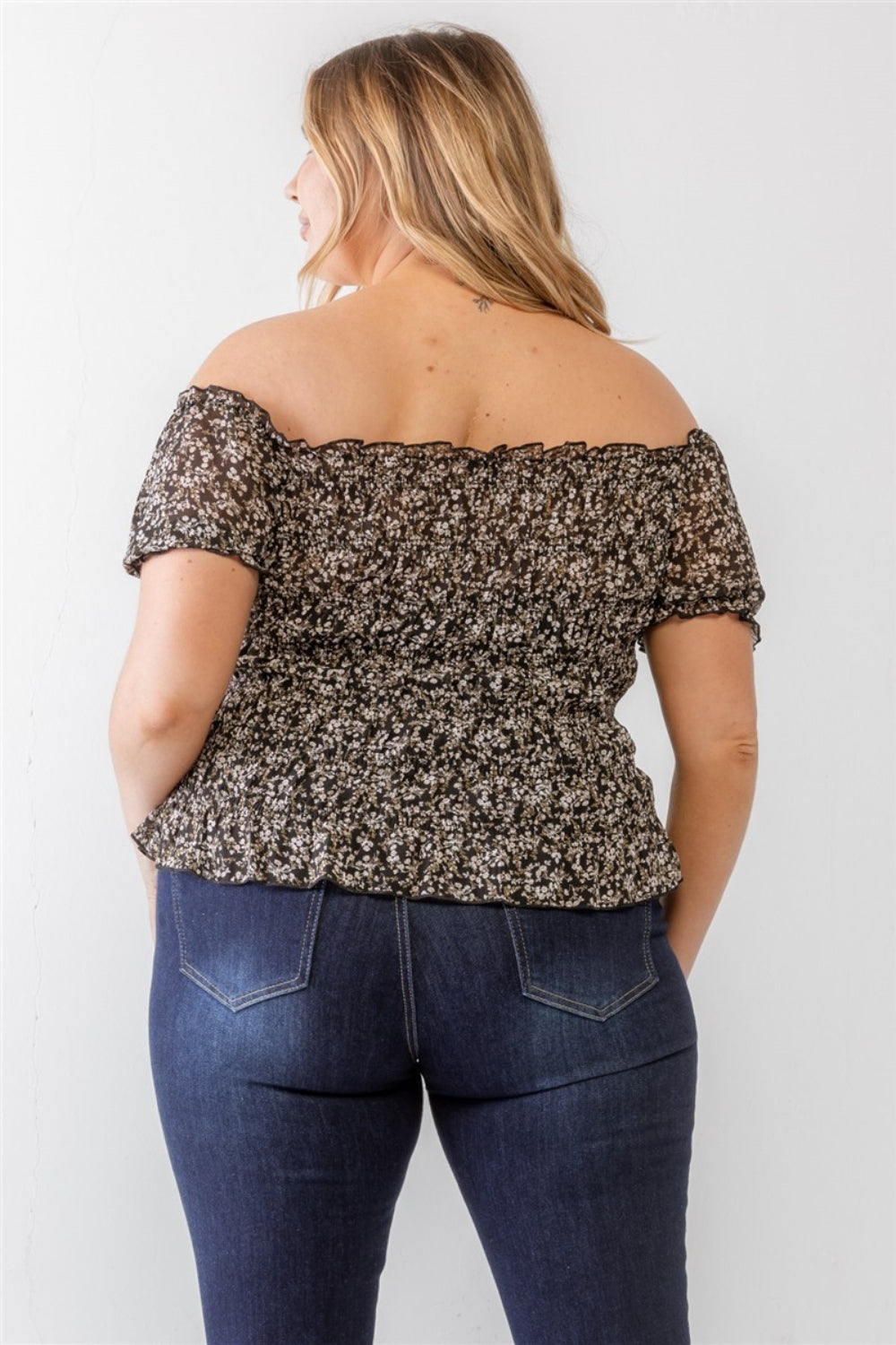 Wearing the Zenobia Plus Size Frill Ruched Off-Shoulder Short Sleeve Blouse and ripped jeans, a person with long hair poses against a plain white background.