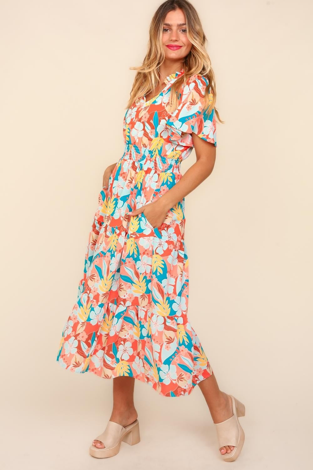 A person wearing the Haptics Full Size Tropical Floral Tiered Dress with Side Pockets and beige platform sandals stands against a plain background.