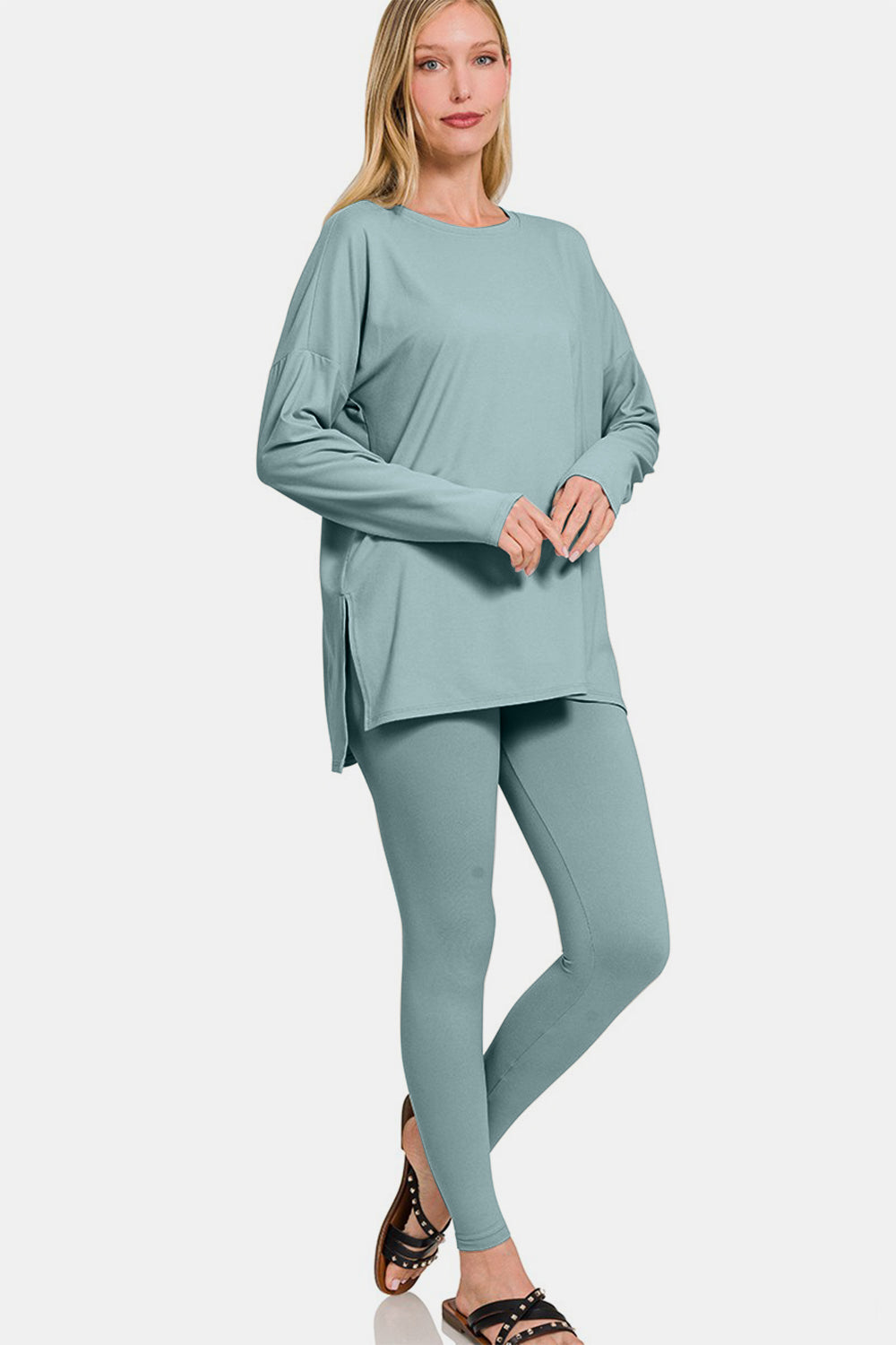 A person wearing the Zenana Full Size Brushed Microfiber Top and Leggings Lounge Set, featuring a loose-fitting teal long-sleeve top and matching stretchy leggings, paired with black sandals, poses against a plain background.