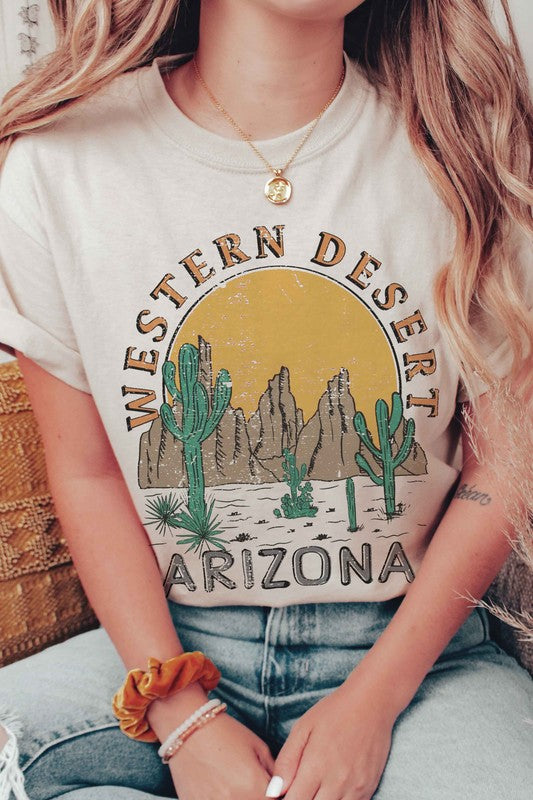 A person wearing the WESTERN DESERT ARIZONA Graphic Tee showcases a bold design featuring cacti and a mountainous landscape against a setting sun. With unisex sizing, this tee is perfect for anyone who loves desert vibes.