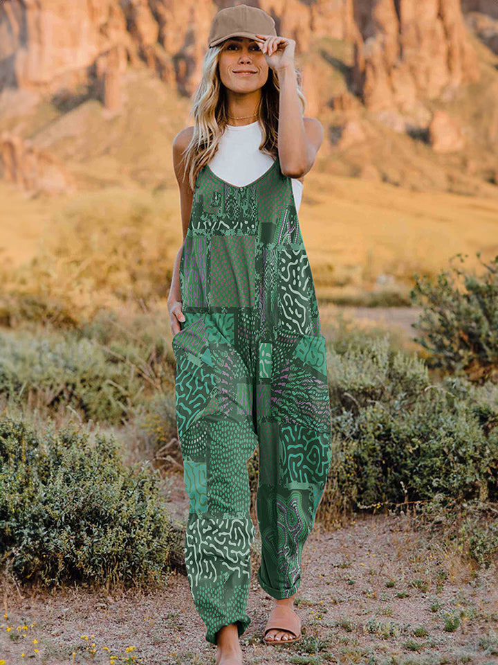 A person standing outdoors in front of rocky terrain, wearing a Full Size Printed V-Neck Sleeveless Jumpsuit and a hat.