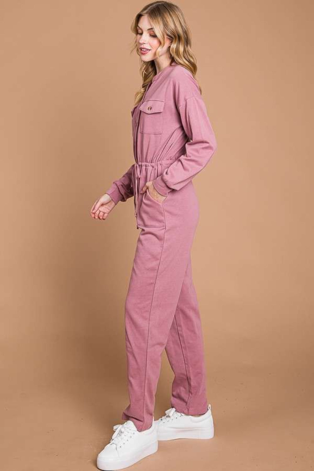 Against a beige background, an individual models the Culture Code Full Size Button Up Drawstring Waist Straight Jumpsuit, which features a stylish pink design with pockets and a chic drawstring waist.