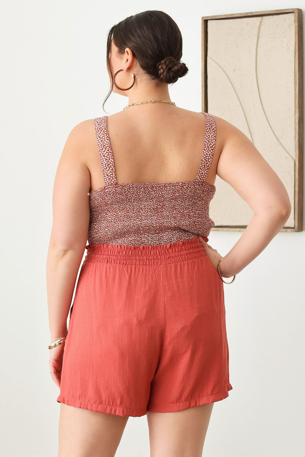 A woman wearing a light green cut-out top and Zenobia Plus Size Drawstring Elastic Waist Shorts with Pockets stands indoors, holding a woven handbag.