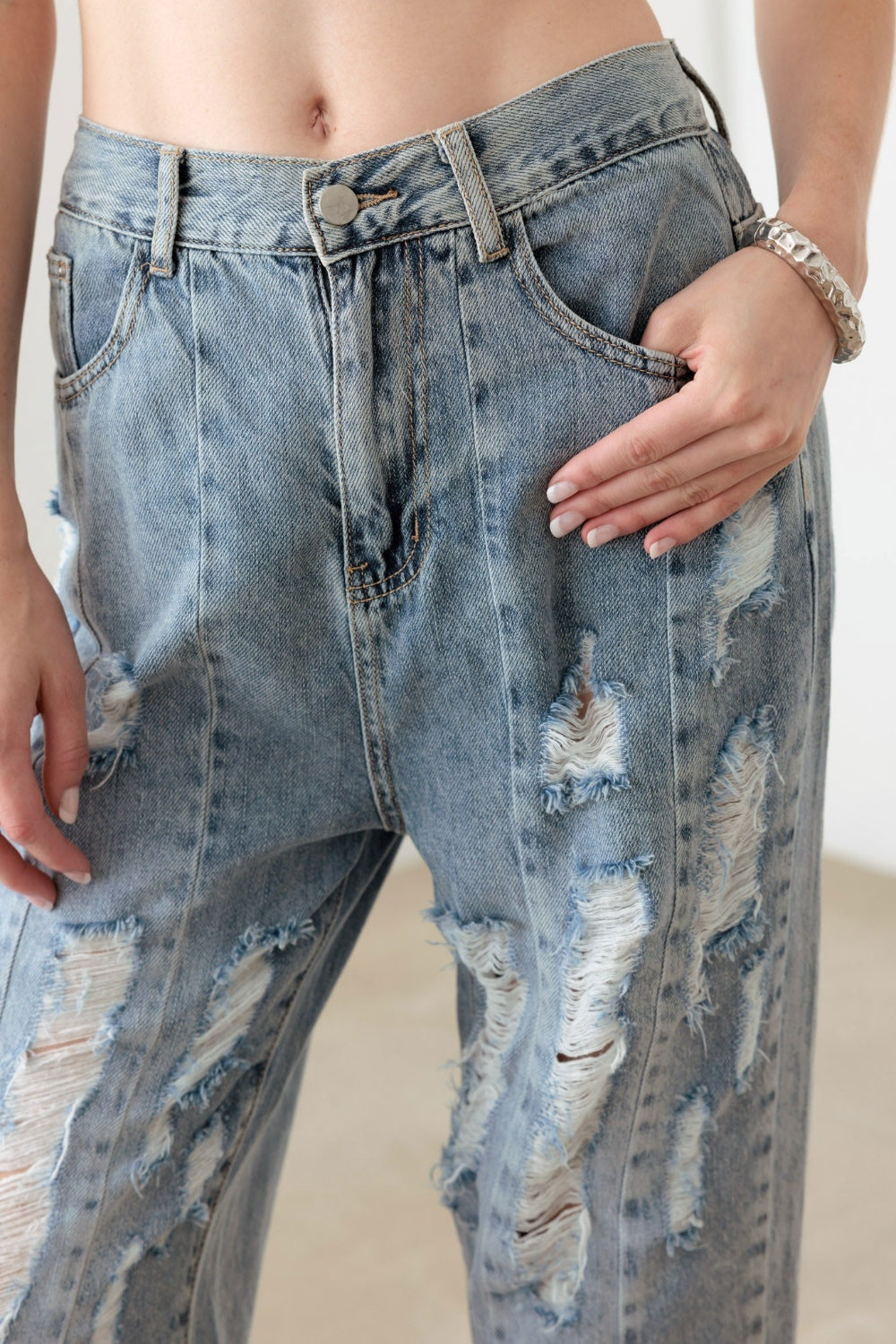 A person wearing Litz La Washed Barrel Leg High Waist Distressed Jeans and white sandals stands on a gray floor against a white wall.